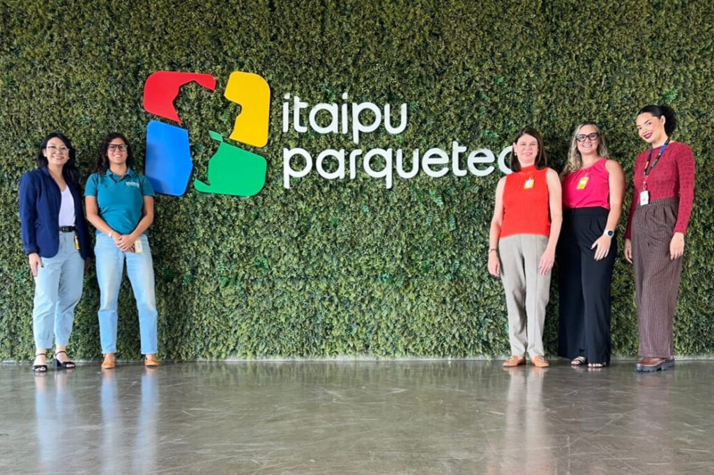 A imagem mostra a comitiva da Inova Unicamp junto com a Camila Clementino em frente a uma parede viva com o logo do Itaipu Parquetec. Fim da descrição.